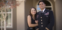 Soldier wearing dress blues standing with parent outside of house during the day.