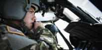 Soldier sitting in cockpit of a Blackhawk helicopter during the daytime.