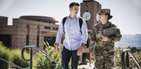 Male ROTC Cadet wearing civilian clothing and a backpack with a female wearing OCP holding books walking up steps outside during the daytime.